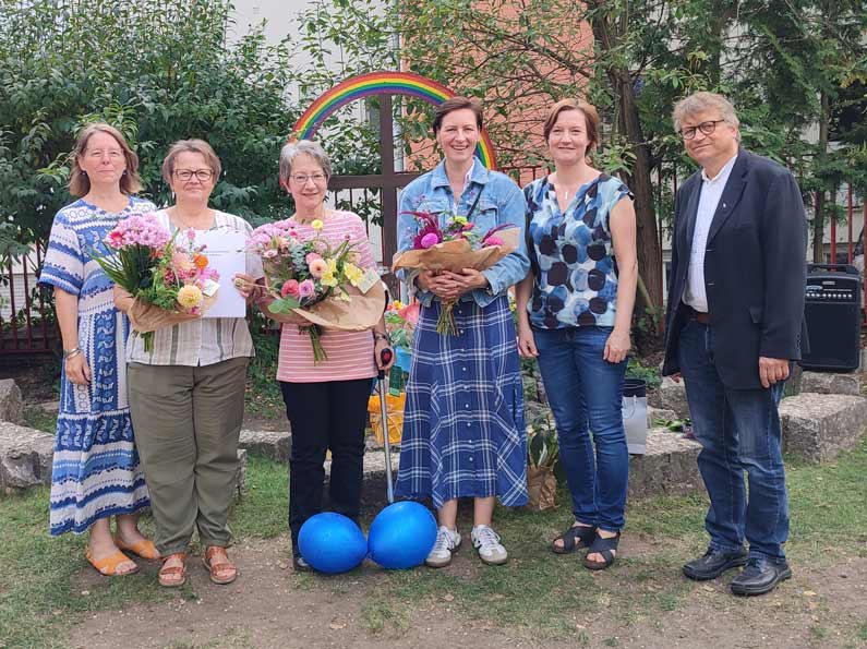 Foto: Sechs Mitarbeiter des Kindergartens verschiedenen Geschlechts stehen im Garten für ein Gruppenfoto